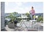Frau reinigt Balkonmöbel mit einem Hochdruckreiniger auf einem Balkon mit Aussicht.