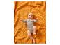 Glückliches Baby in einem grauen Body auf einer orangefarbenen Waffeldecke liegend.