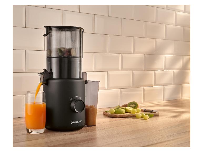 Schwarzer Entsafter bereitet Orangensaft zu, mit frischem Obst auf dem Tisch.