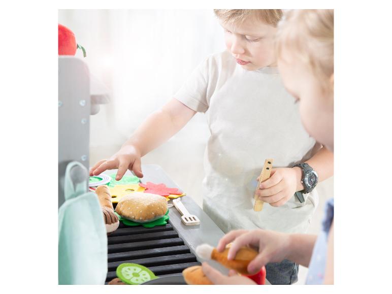 Kinder spielen mit einem Spielzeuggrill und Filzessen, darunter ein Burger und Gemüse.