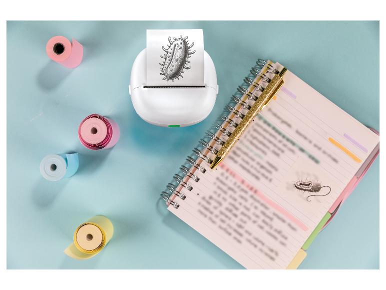 Weißer Minidrucker mit Bakterienausdruck, Notizbuch und Stift auf blauem Hintergrund.