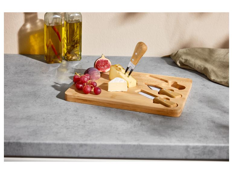 Holz-Käseplatte mit Käse, Feigen, Trauben und Messern auf einer Arbeitsplatte.