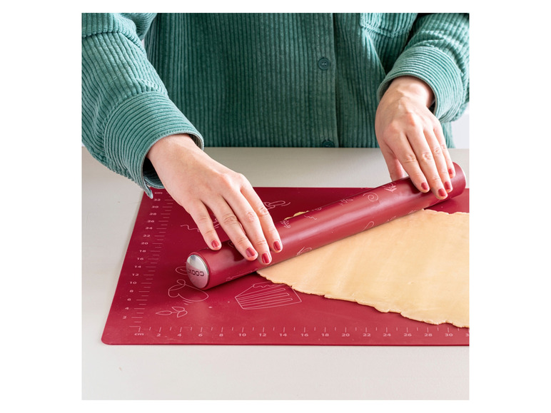 Ein roter Nudelholz auf einer roten Backmatte mit Teig.