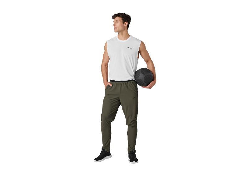 Mann in weißem ärmellosem Oberteil und khakifarbener Trainingshose, der einen schwarzen Medizinball hält.