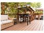 Schwarzer Gasgrill mit zwei Propangasflaschen auf einer Holzterrasse mit Sofa und Pergola.