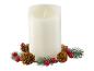 Eine weiße Kerze mit Flammeneffekt, umgeben von Tannenzweigen, Zapfen und roten Beeren.