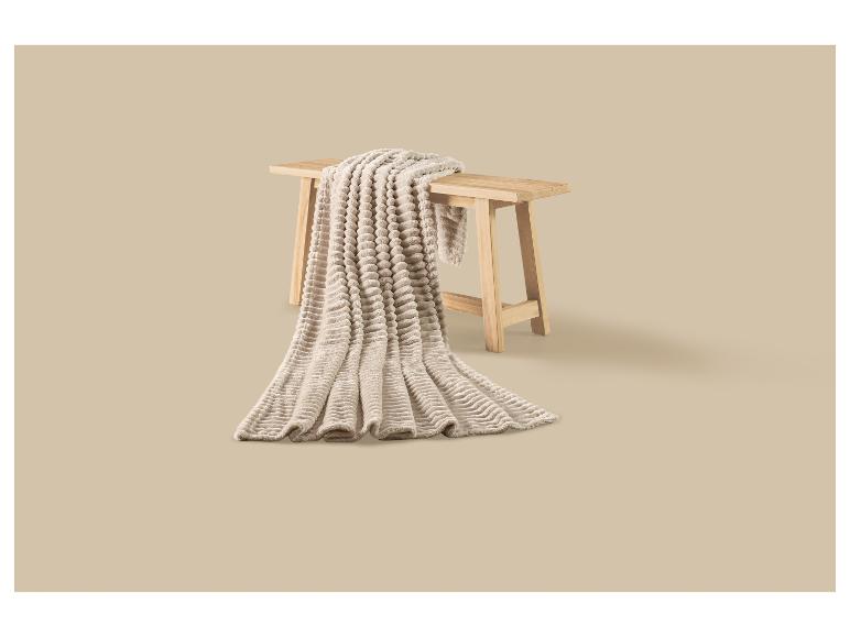 Beige, weiche Decke mit Blasenstruktur über einer Holzbank drapiert.