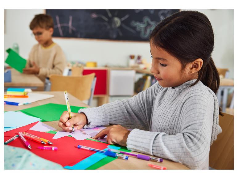 Mädchen zeichnet mit einem Goldstift an einem Tisch mit farbigem Papier im Klassenzimmer.