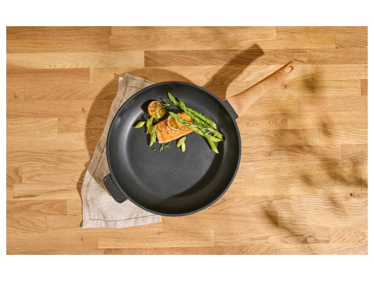 Pfanne mit Lachs, Spargel und Zitrone auf einem Holztisch.