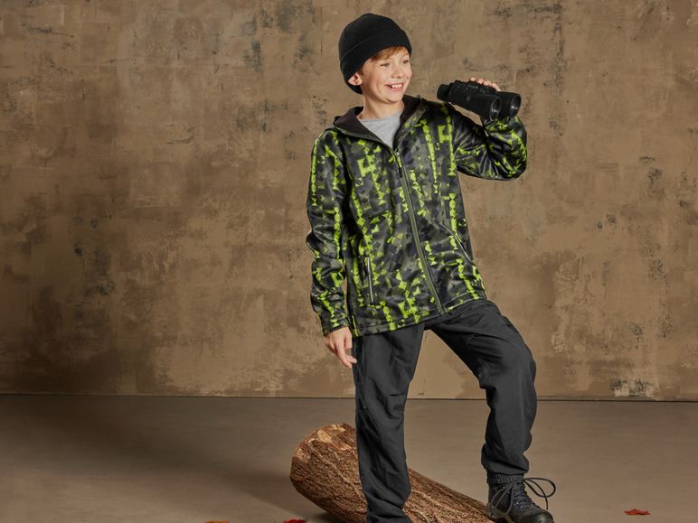 Ein Junge trägt eine Camouflagejacke und eine schwarze Hose und schaut durch ein Fernglas.