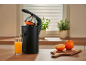 Elektrische Zitruspresse presst frischen Orangensaft in ein Glas auf einem Holztisch