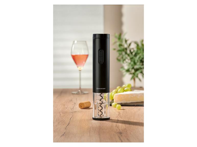 Schwarzer elektrischer Korkenzieher auf Holztisch mit Wein, Käse und Trauben im Hintergrund.