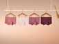 Vier Paar rosa Unterhosen mit Punkten, Streifen und uni, die an einer Holzleiste hängen.