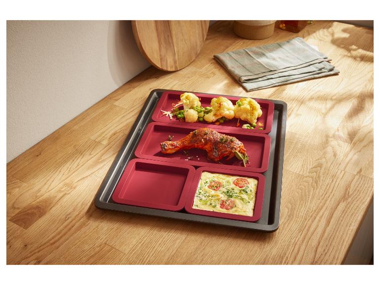 Backblech mit roten Silikon-Einsätzen, enthaltend gebratenes Hähnchen und Gemüse.