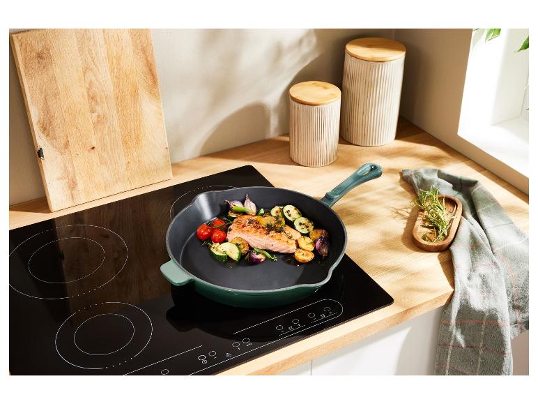 Eine grüne Pfanne mit Lachs und Gemüse auf einem Induktionskochfeld.