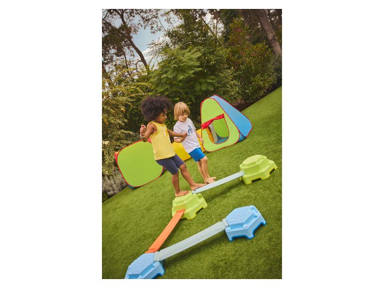 Kinder spielen auf einem Balancierbalken im Freien mit Spielzelten.