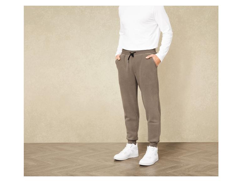Mann trägt ein weißes Longsleeve und braune Jogginghose mit weißen Sneakern.