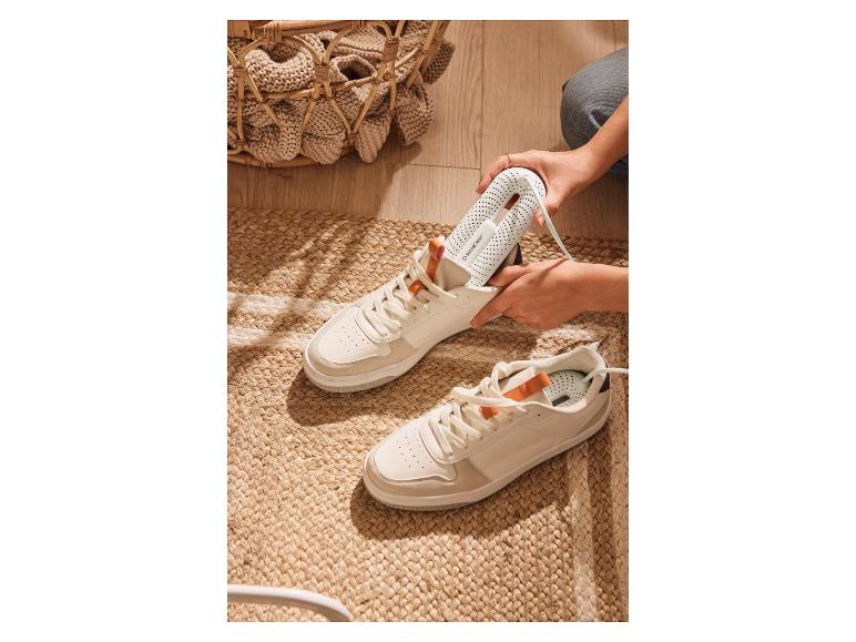 Eine Person steckt einen weißen Schuhtrockner in einen weißen Sneaker auf einem gewebten Teppich.