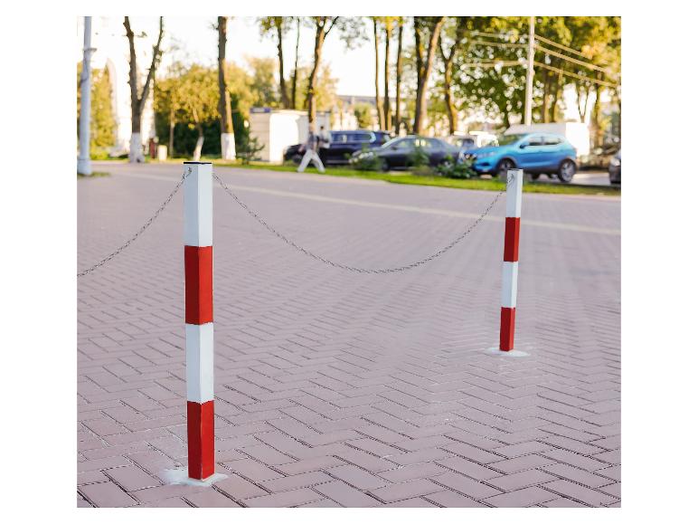 Zwei rot-weiße Poller mit einer Kette auf einem gepflasterten Gehweg, mit Autos im Hintergrund.