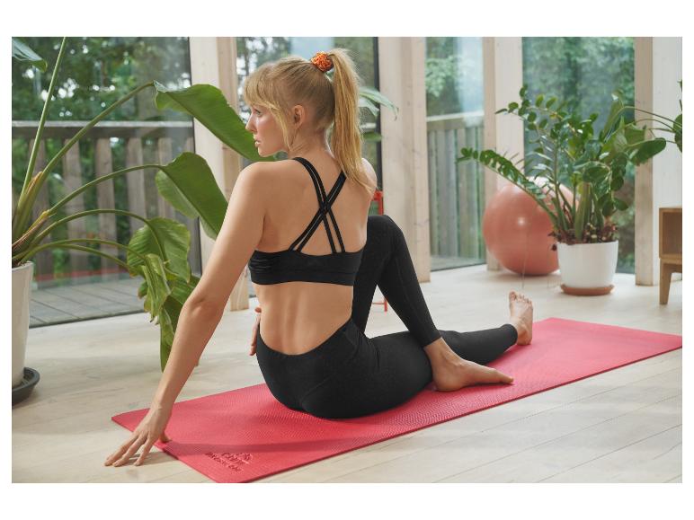 Frau in schwarzen Leggings und Sport-BH macht Yoga auf einer roten Matte.