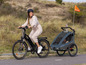 Eine Frau fährt ein E-Bike mit einem Qeridoo Kinderanhänger.