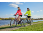 Ein Mann und eine Frau fahren auf einem gepflasterten Weg am Wasser Fahrrad.