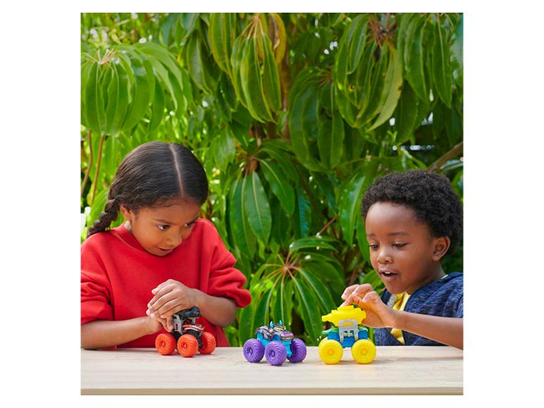 Zwei Kinder spielen draußen mit bunten Monstertruck-Spielzeugen auf einem Holztisch.