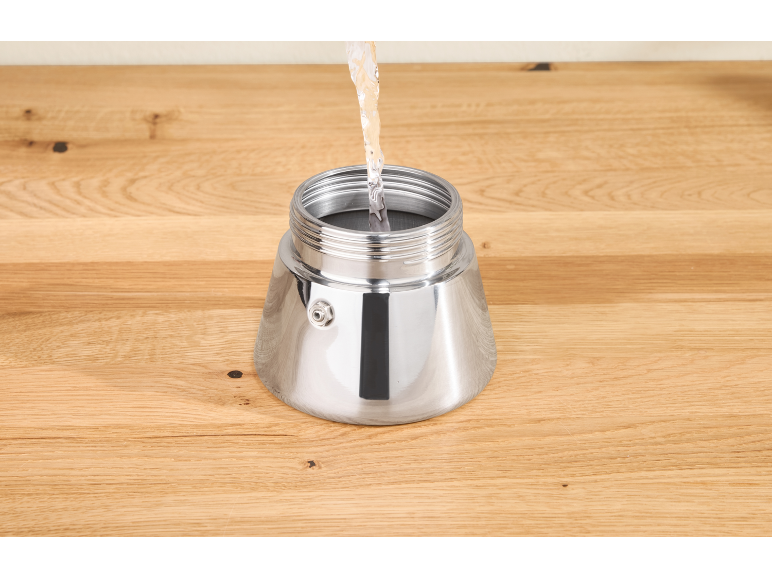 Wasser wird in den silbernen Boden einer Kaffeemaschine auf einem Holztisch gegossen.
