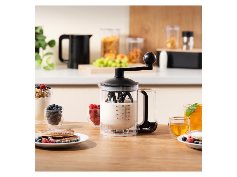 Teigspender mit Kurbel, Pfannkuchen und Beeren auf einem Holztisch.