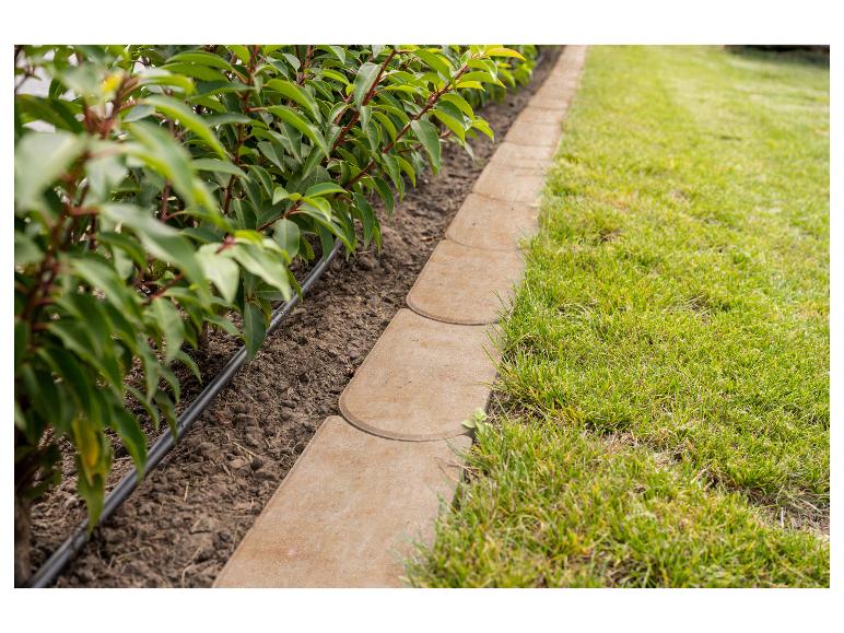 Steinerne Gartenbegrenzung, die ein Pflanzenbeet und einen Rasen trennt.