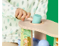 Kleinkind spielt mit einem Holzspielzeug mit Hammer und Bällen, gekleidet in einen Strampler mit Regentropfenmuster.