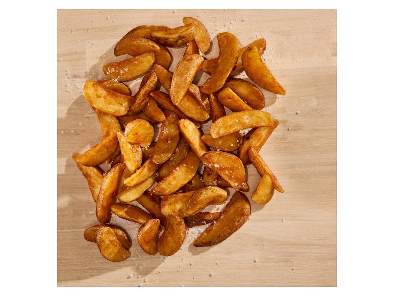 Goldene, knusprige Kartoffelspalten mit Meersalz auf Holzuntergrund.