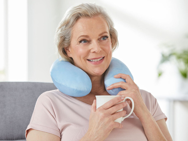 Eine Frau mit einem blauen Nackenkissen hält eine weiße Tasse.