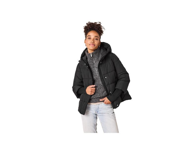 Frau in schwarzer Steppjacke, grauem Pullover und heller Jeans.