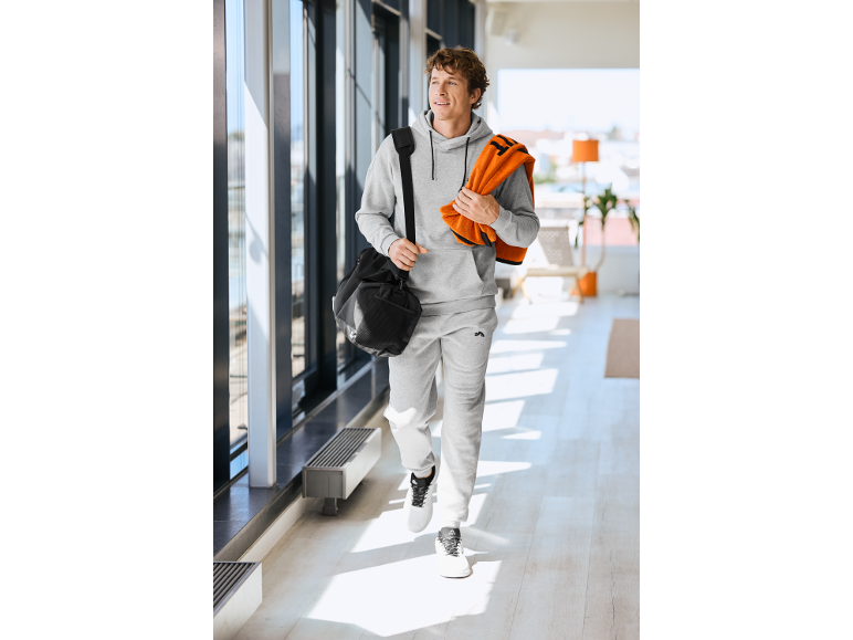 Mann im grauen Trainingsanzug mit einer Sporttasche und einem orangefarbenen Handtuch.