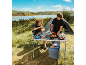 Paar kocht an Campingtisch und Kühlbox am See.