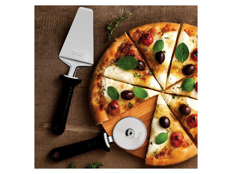 Pizza mit Tomaten, Oliven und Basilikum, mit Pizzaschneider und -heber auf Holzbrett.