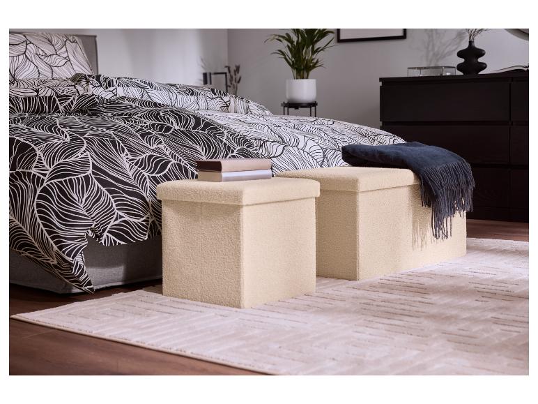 Schlafzimmer mit schwarz-weißem Bettbezug mit Blattmuster, zwei beigen Aufbewahrungshockern und einem Teppich.