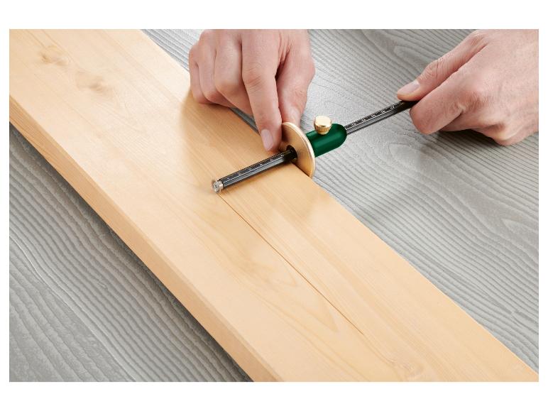 Eine Hand benutzt ein kreisförmiges Holzwerkzeug, um eine Linie auf einem Holzbrett zu markieren.