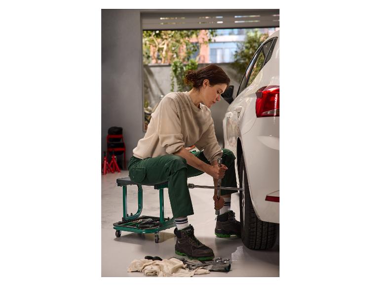 Eine Frau sitzt auf einem PARKSIDE Werkstatt-Rollsitz, während sie einen Autoreifen wechselt.