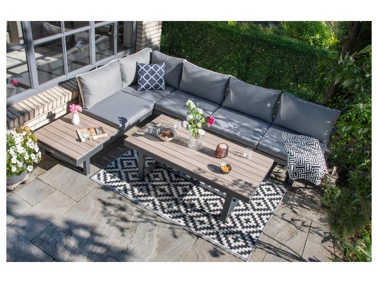Gartenmöbel-Set mit grauen Kissen, zwei Couchtischen und einem schwarz-weißen Teppich.