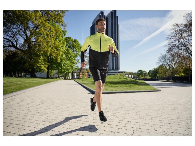 Mann läuft in einem Park, trägt eine zweifarbige Laufjacke und schwarze Shorts.