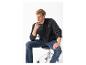Mann in schwarzer Bomberjacke und blauen Jeans, auf einem Stuhl sitzend.