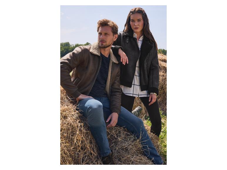 Zwei Models in braunen und schwarzen Shearling-Jacken posieren auf einem Heufeld.