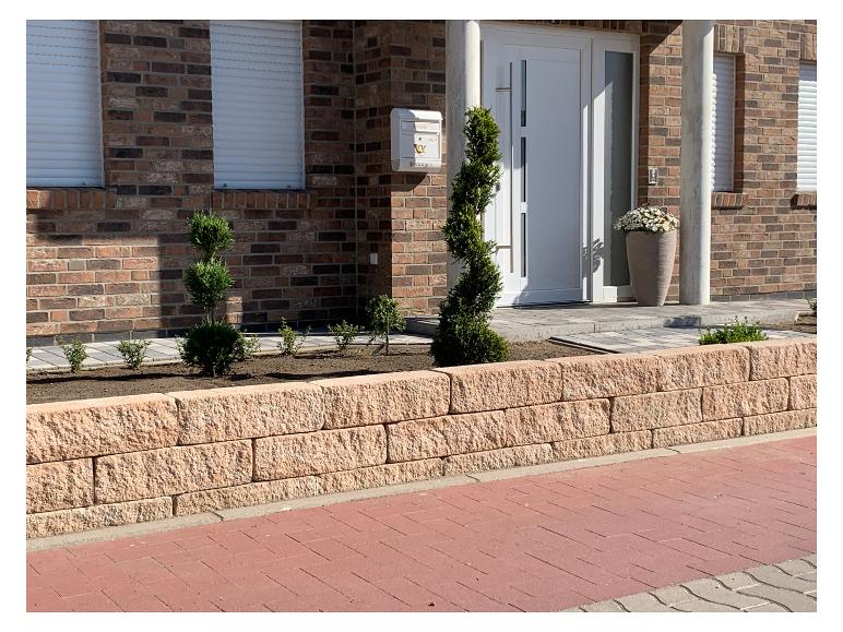 Ziegelhausfassade mit weißer Tür, Pflanzgefäßen und gepflasterter Auffahrt.