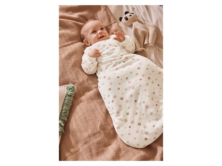 Baby in Sternen-Schlafsack, auf Decke liegend mit Panda-Stofftier.