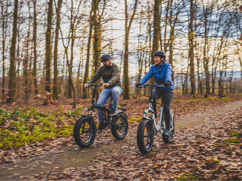 Zwei Personen fahren mit E-Bikes durch einen Wald.