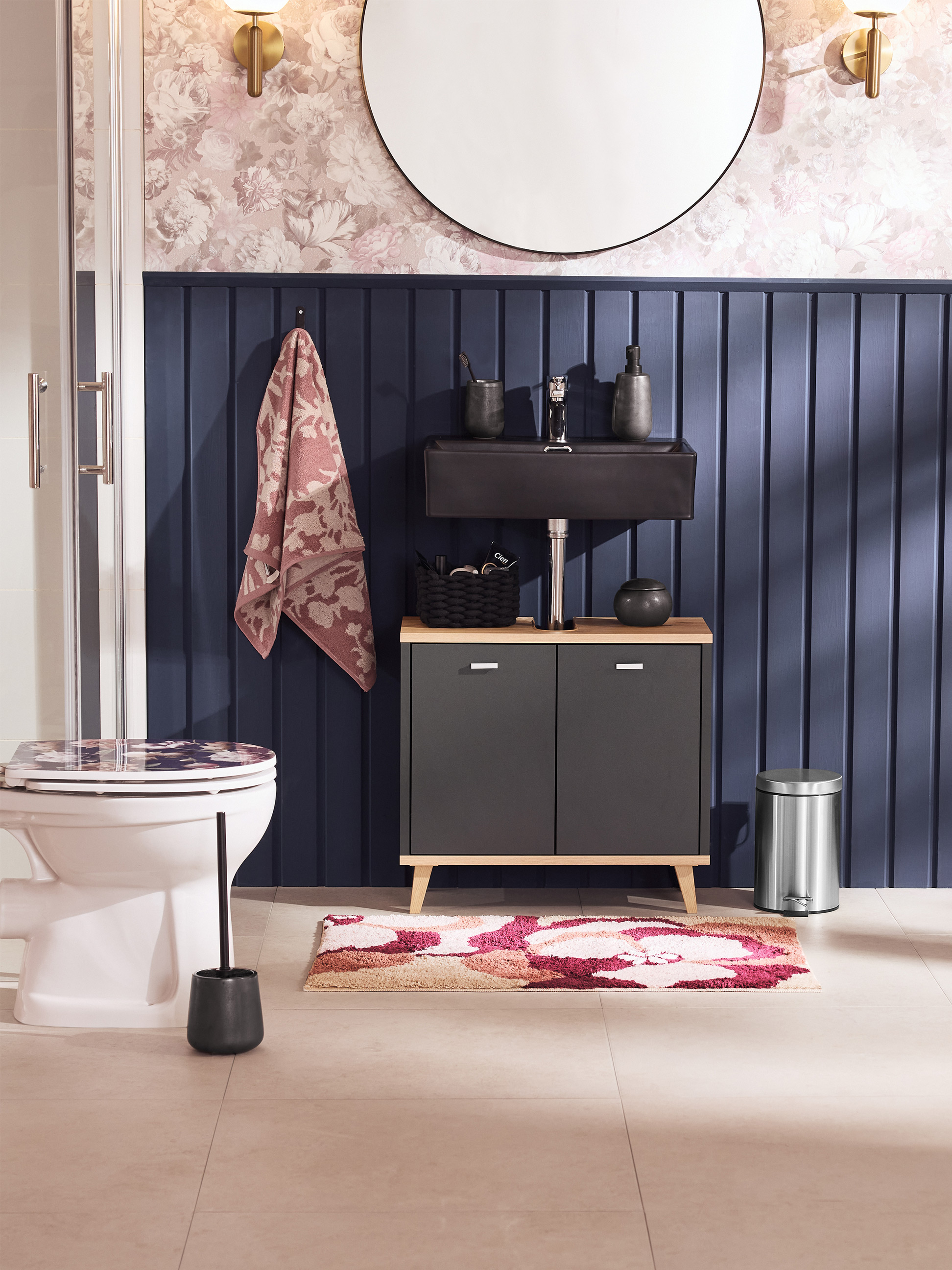 Badezimmer mit Toilette, Waschbecken, Schrank und floralem Teppich.