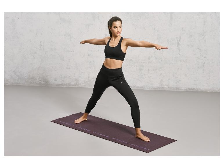 Eine Frau in schwarzer Sportbekleidung macht Yoga auf einer lila Matte von Jette Sport.