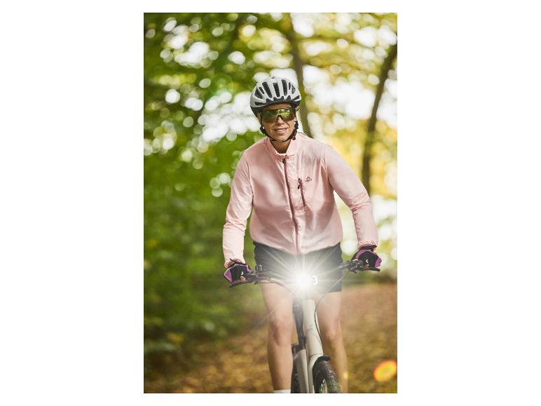 Lächelnde Frau auf E-Bike mit Helm und Sonnenbrille, trägt eine pinke Crivit Jacke.